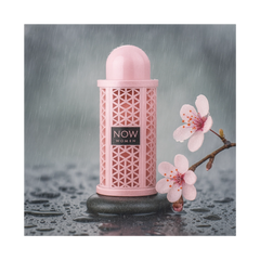 Now Women Rave 100ml EDP by Lattafa, elegantly displayed with pink flowers on a wet stone surface.